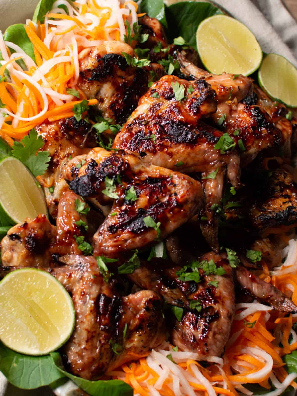 Nicely charred chicken wings on a platter with pickled salad and fresh limes. 