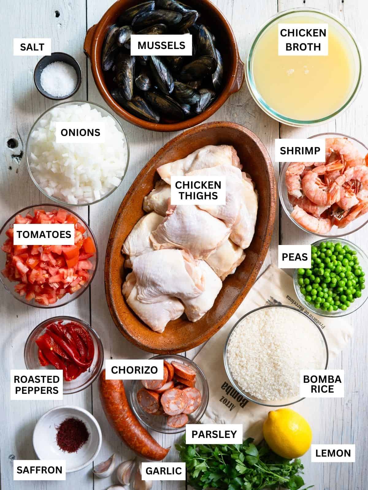 all ingredients to make paella mixta are laid out and labeled on a white background. 