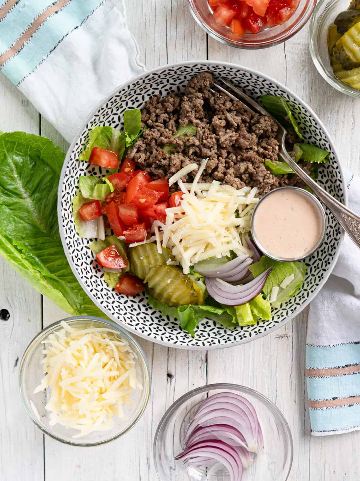 a bowl filled with lettuce, ground beef, tomatoes, onions, pickles and special sauce with a fork. 