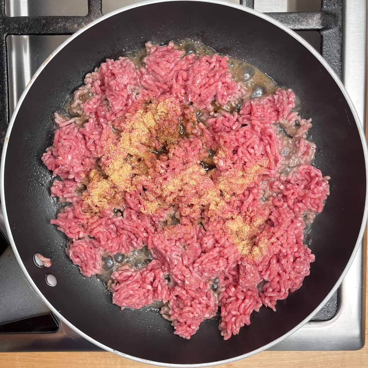 raw ground beef in a frying pan with spices on top.