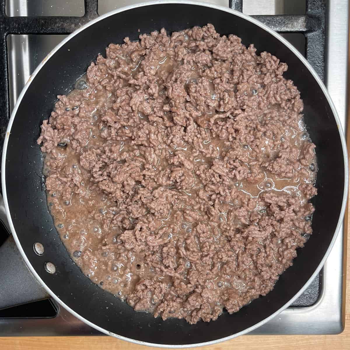 cooked ground beef in a frying pan showing that liquid has been released from the meat. 