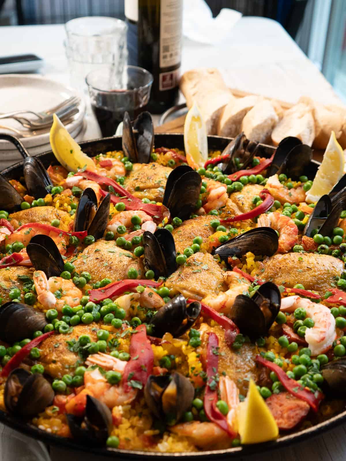 close up of finished paella with a bottle of wine and sliced bread in the background.