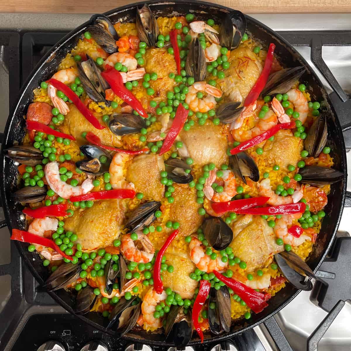 after the rice is cooked the paella is decorated with green peas and red pepper strips.