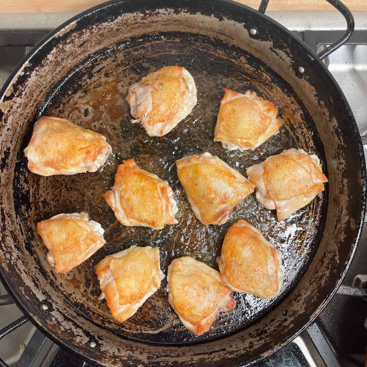 10 chicken thighs browning in a paella pan.