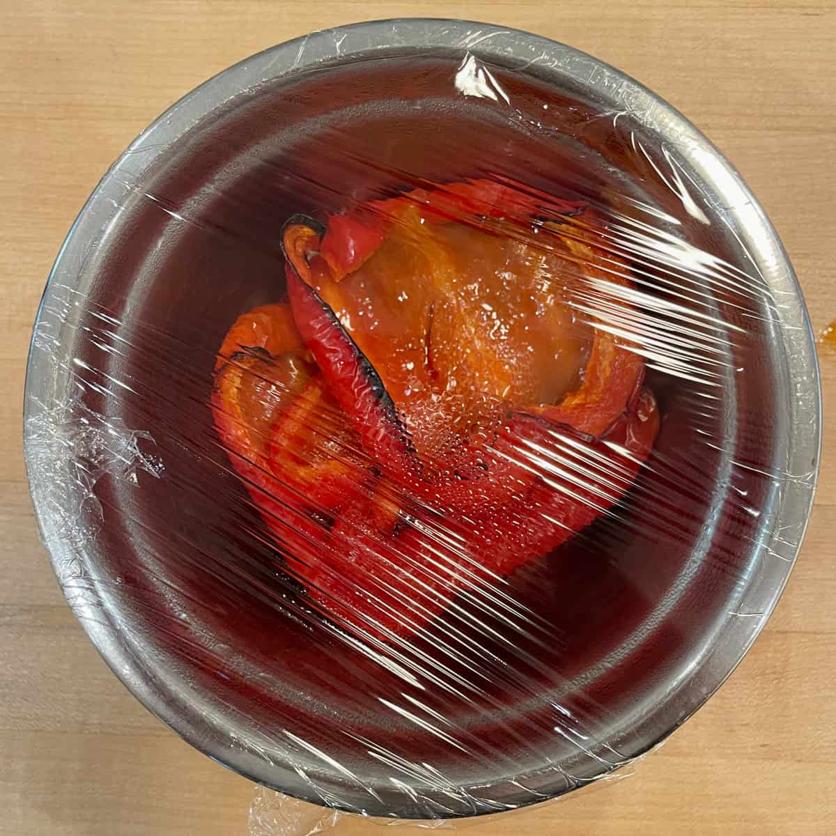 Roasted peppers in a bowl covered with plastic wrap.