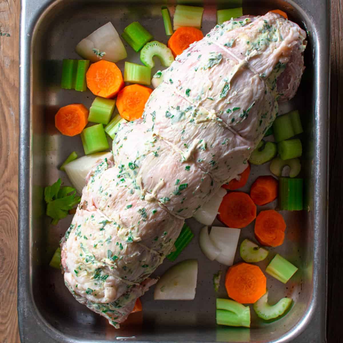 rolled turkey breast in a roasting pan on a bed of carrots, celery and onions ready to be baked. 