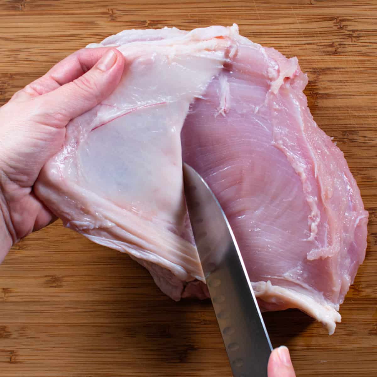 a knife cutting the skin from a turkey breast. 