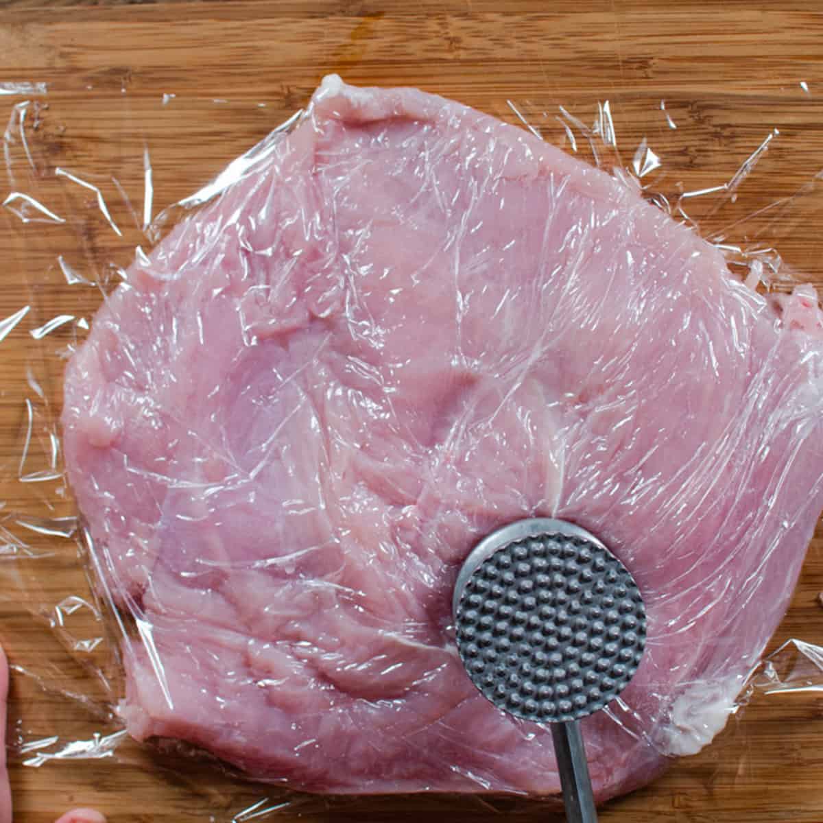 A turkey breast is being flattened with a mallet. 