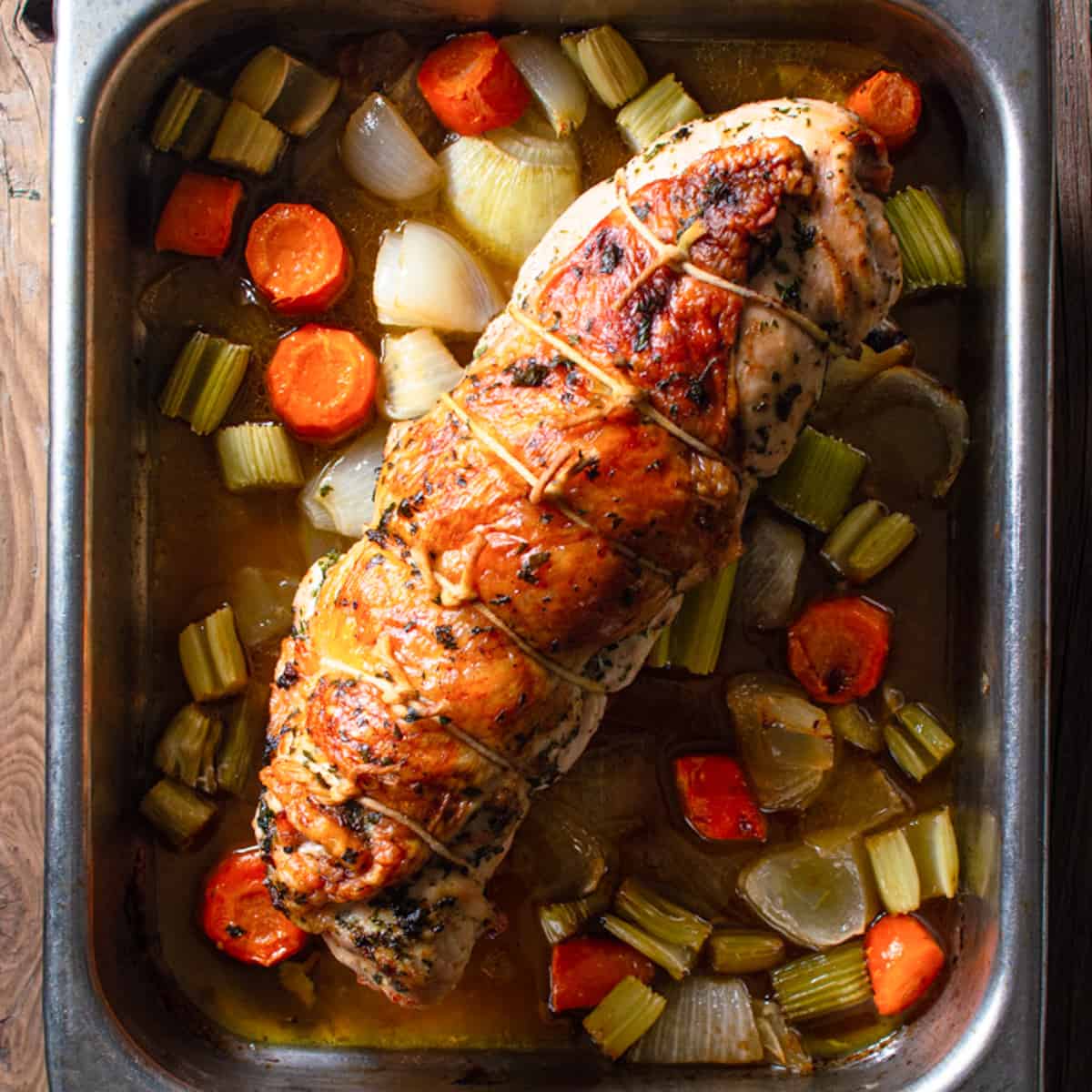 roasted stuffed turkey breast on top of a bed of carrots and celery.