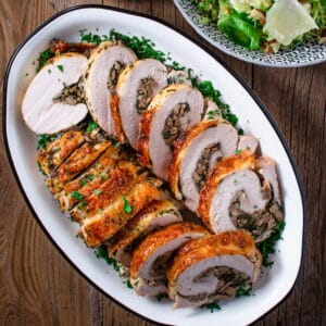 Slices of stuffed turkey breast laid out on an oval platter with a salad on the side.