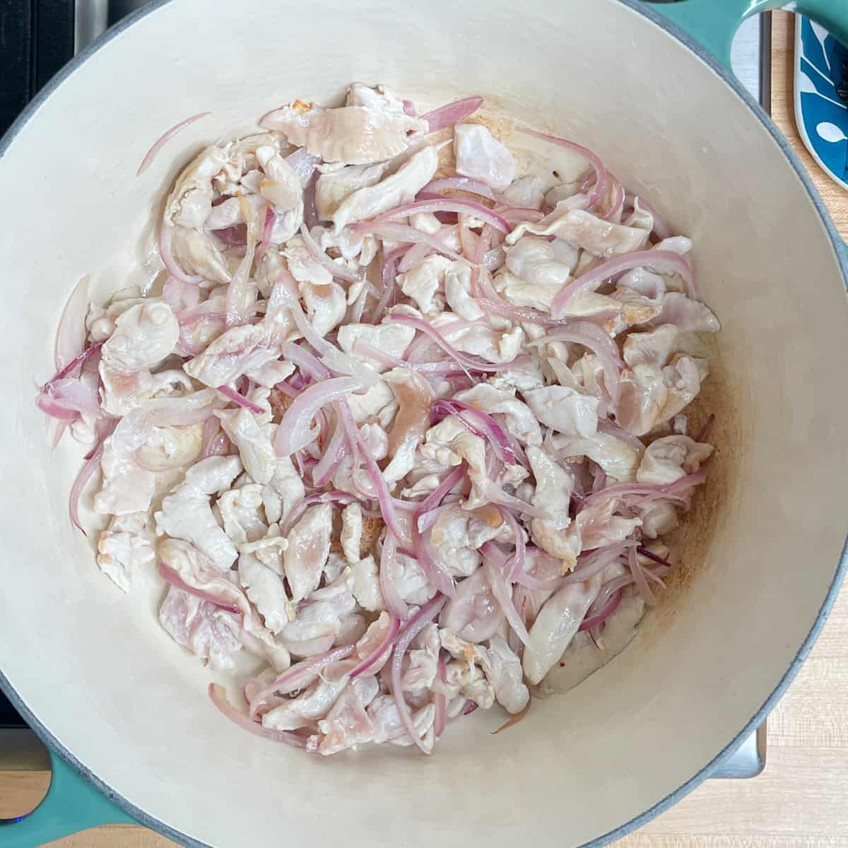 chicken pieces and red onion slices frying in a soup pot. 