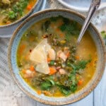 one bowl of white bean soup garnished with fresh Parmesan cheese. A spoon rests in the bowl.