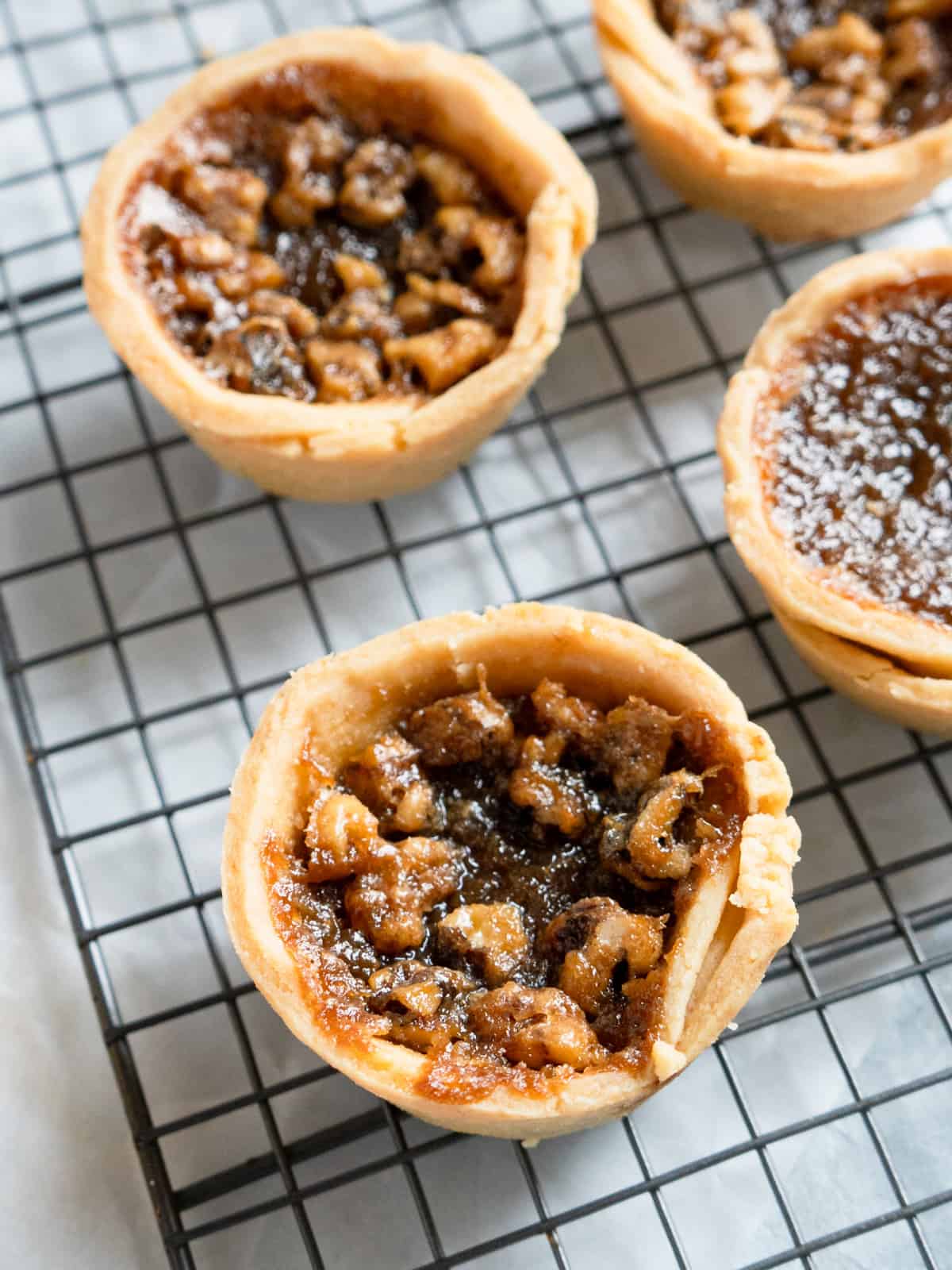 close up of one butter tart with walnuts. 3 more tarts in the background.