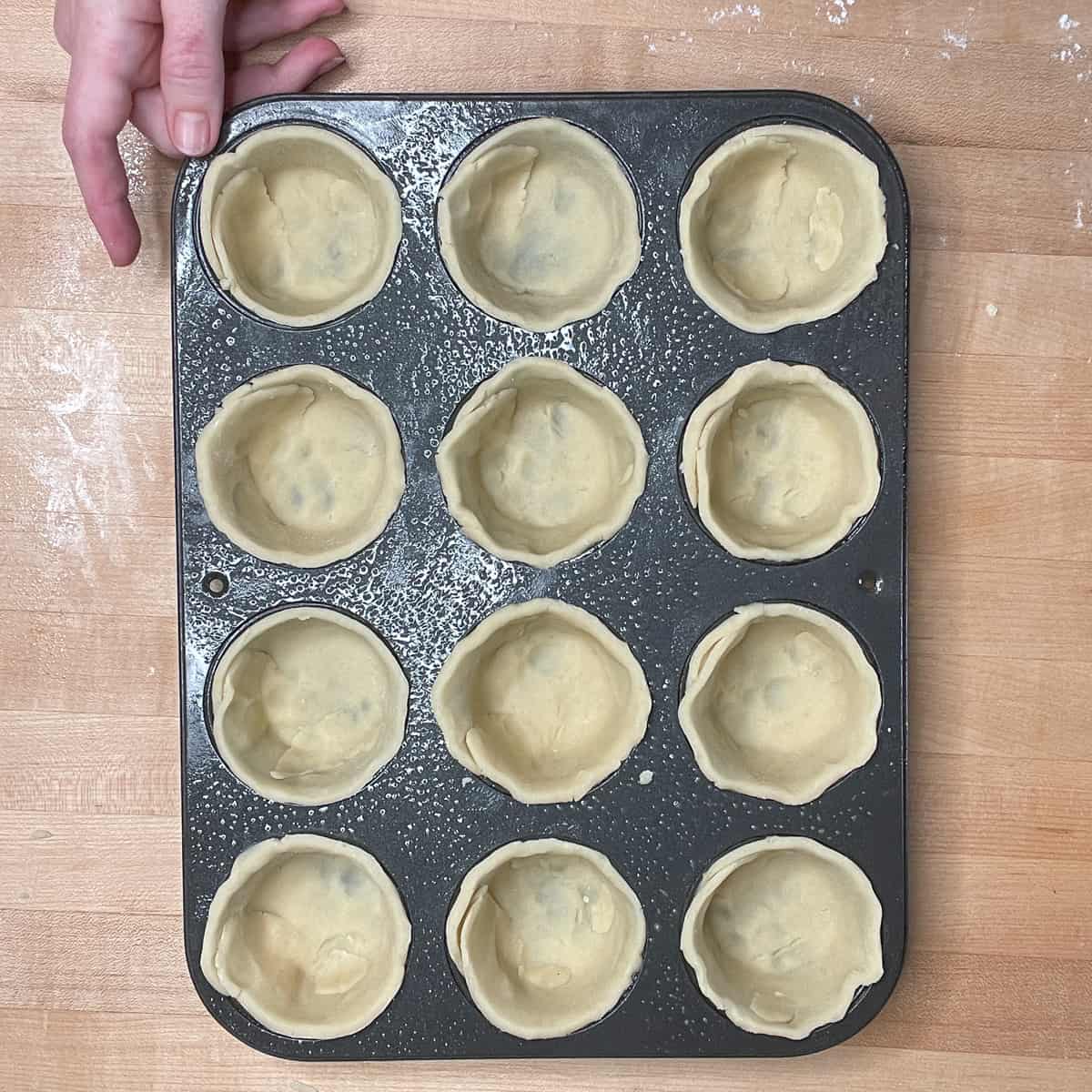 12 unfilled tart shells in a muffin tin.