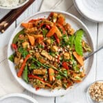 A large platter of tofu stir fry with a serving spoon and chopsticks on the side.