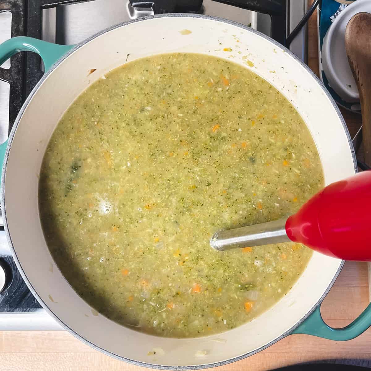 a soup pot with broccoli soup being pureed with a hand immersion blender.