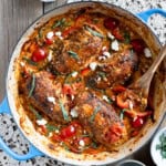 Harissa baked chicken in a blue brasier with a serving spoon. Small dishes of garnishes on the side.