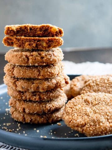 Stack of ginger cookies with one broken in half on the top showing chunks of candied ginger.