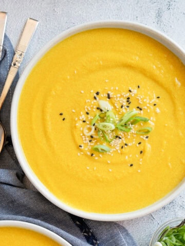 one bowl of miso butternut squash soup garnished with sliced green onions and black and white sesame seeds.