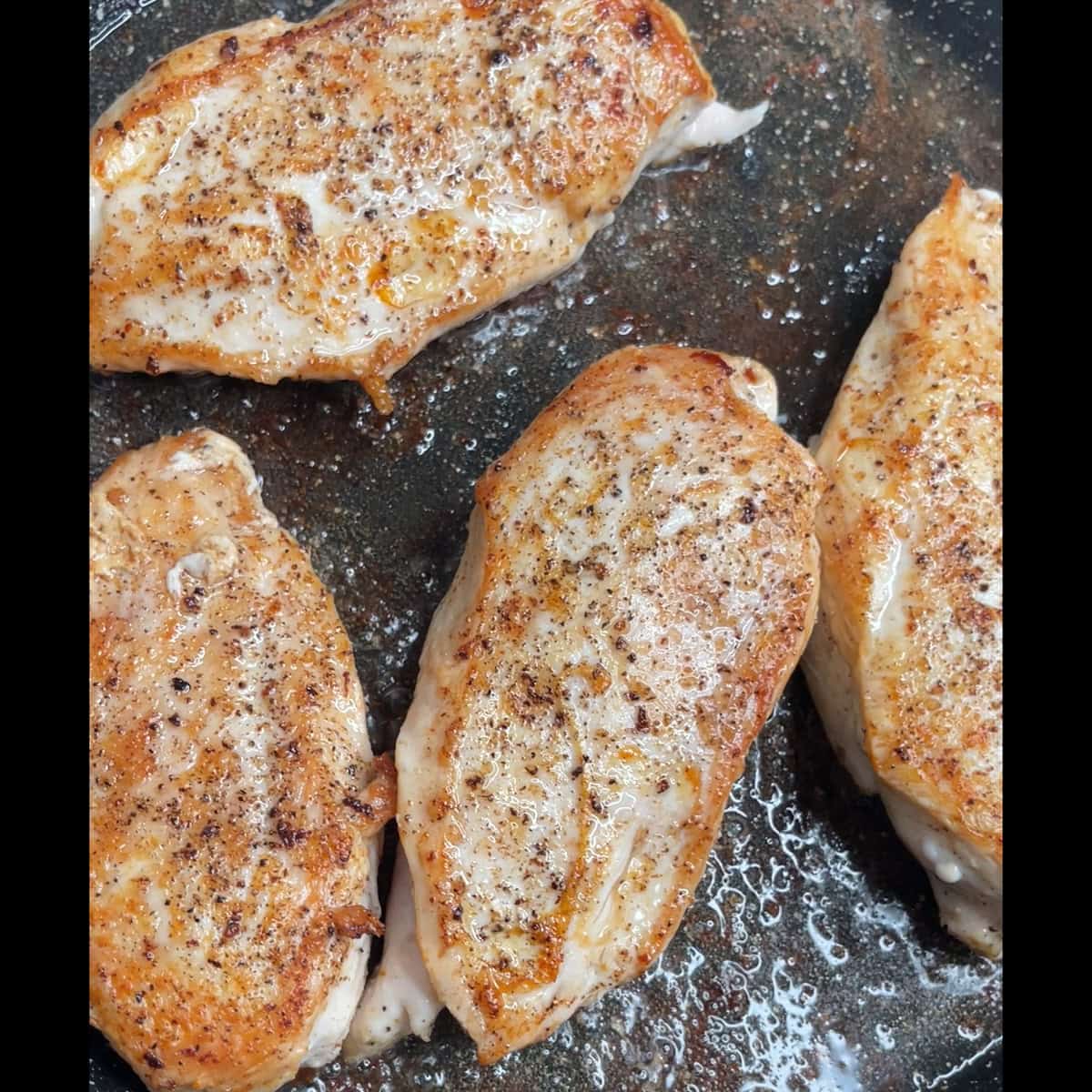 Boneless chicken breasts browned in a pan.