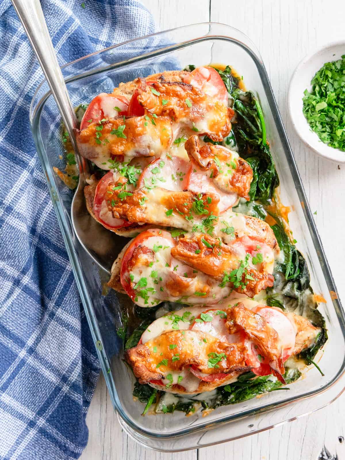Chicken club bake in a casserole dish with a serving spoon and a blue towel in the background.