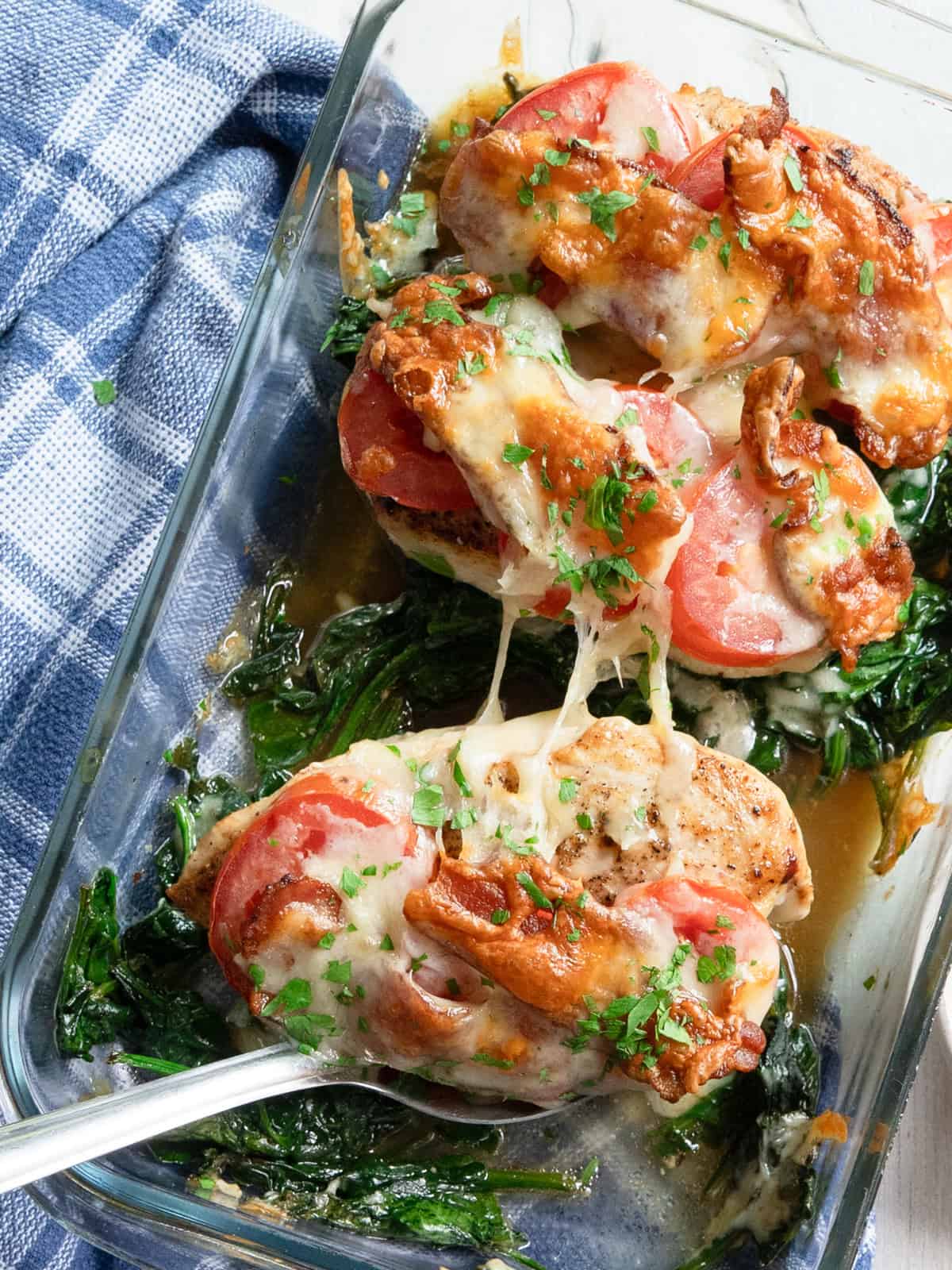 One chicken club breast on a serving spoon being lifted out of a casserole dish.