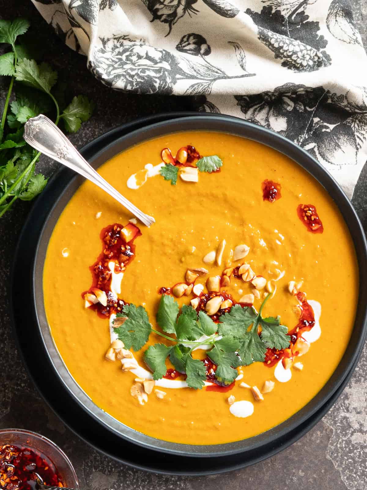 a single bowl of spicy pumpkin and peanut soup with a spoon and garnished with fresh herbs and cream.