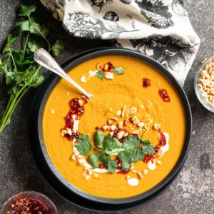 A big bowl of pumpkin peanut soup on a stone slab garnished with fresh cilantro and chili crisp.