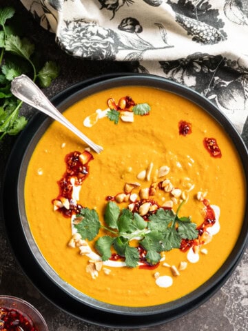 A big bowl of pumpkin peanut soup on a stone slab garnished with fresh cilantro and chili crisp.