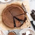 A flourless chocolate souffle cake with 3 slices cut and one on a plate topped with whipped cream.