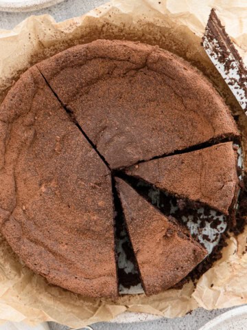 Chocolate souffle cake dusted with cocoa powder with 2 slices cut into it.