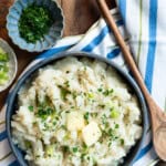 Potato turnip mash in a blue ceramic dish garnished with fresh parsley and sliced green onions.