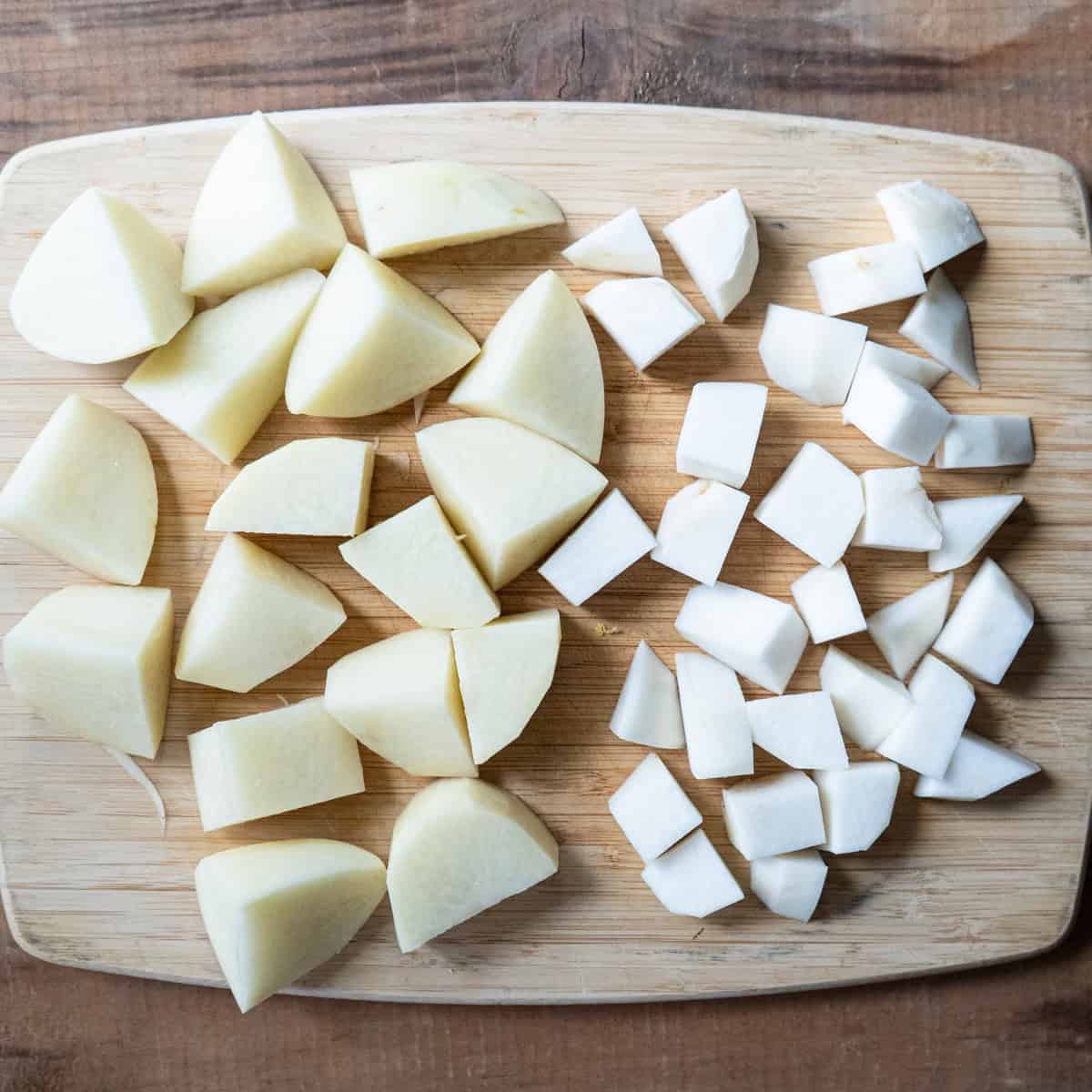 Larger cut potatoes beside smaller cut turnip on a cutting board.