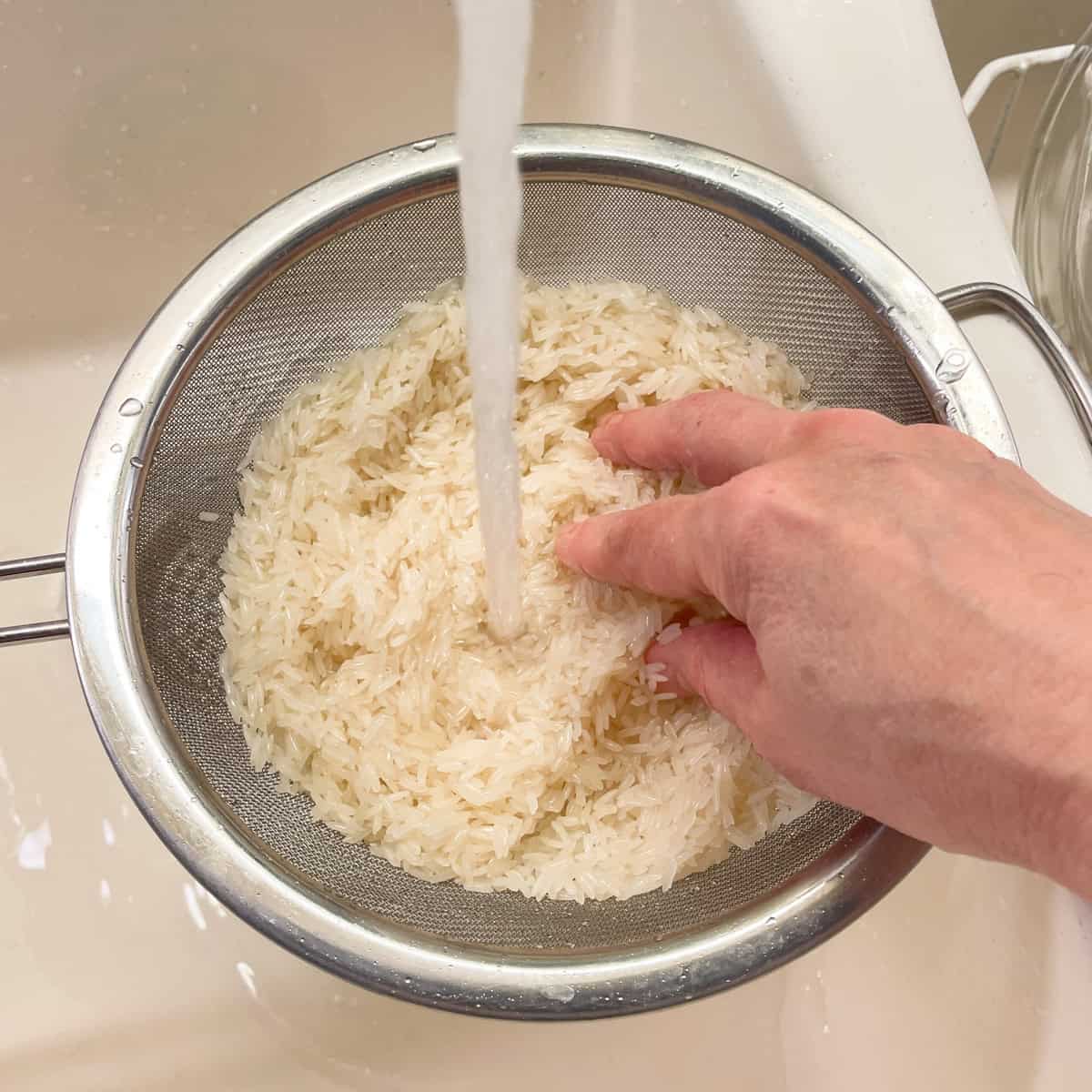 Rinsing jasmine rice in a fine sieve over the sink.