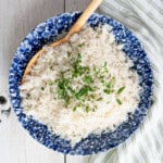 Coconut jasmine rice in a blue and white dish. It's garnished with cilantro and a wooden serving spoon.