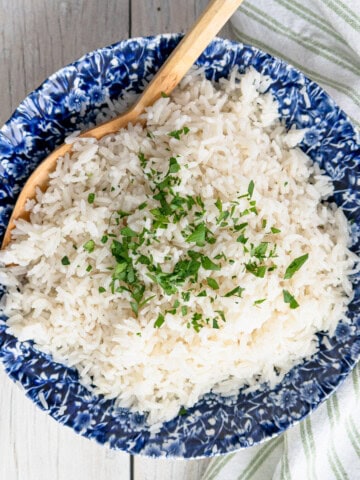 Coconut jasmine rice in a blue and white dish. It's garnished with cilantro and a wooden serving spoon.