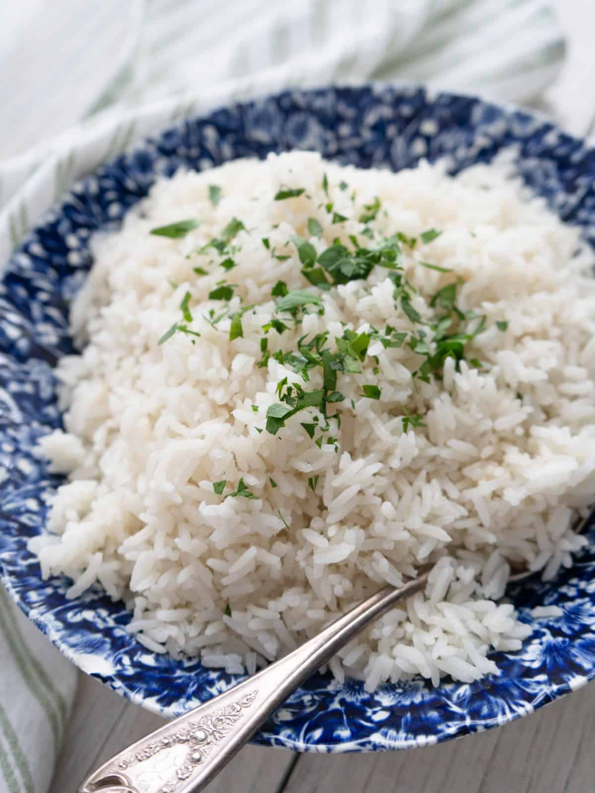 Coconut jasmine rice in a blue bowl with a serving spoon and garnished with chopped fresh cilantro.