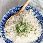 Coconut jasmine rice in a blue and white bowl with a wooden serving spoon. Chopped cilantro is sprinkled on top.