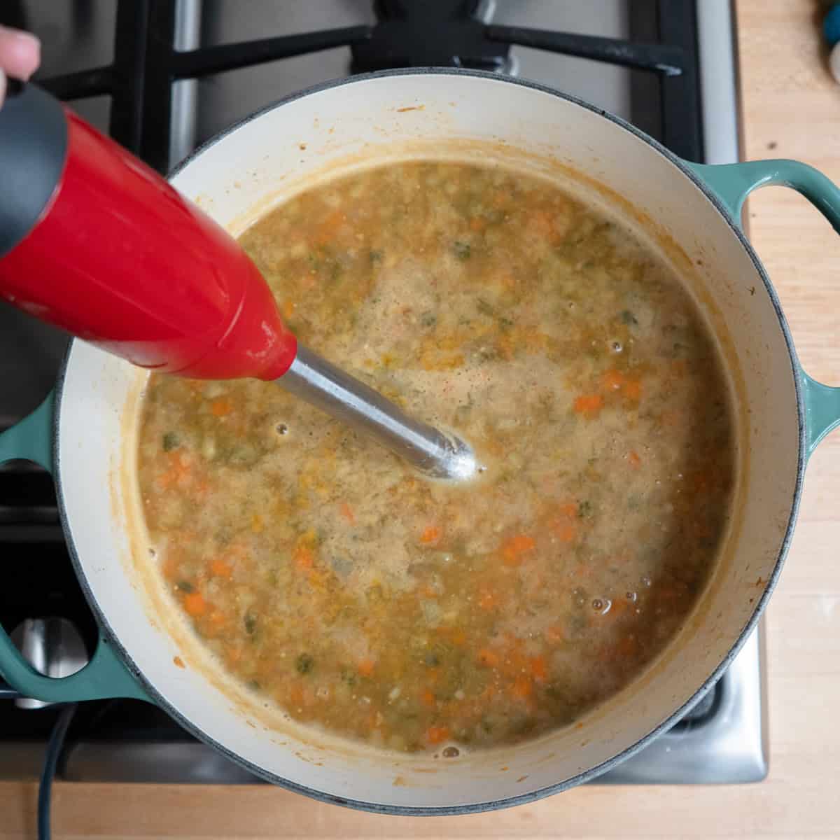 Blending dill pickle soup with an immersion blender.