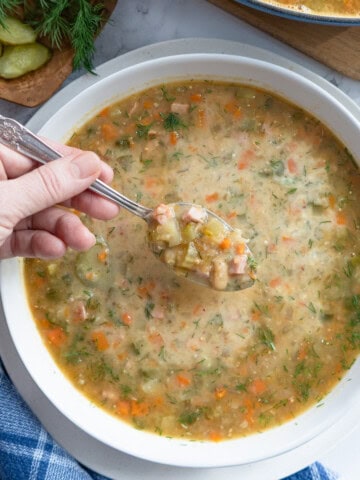 A bowl of dill pickle soup with a spoonful being scooped up.