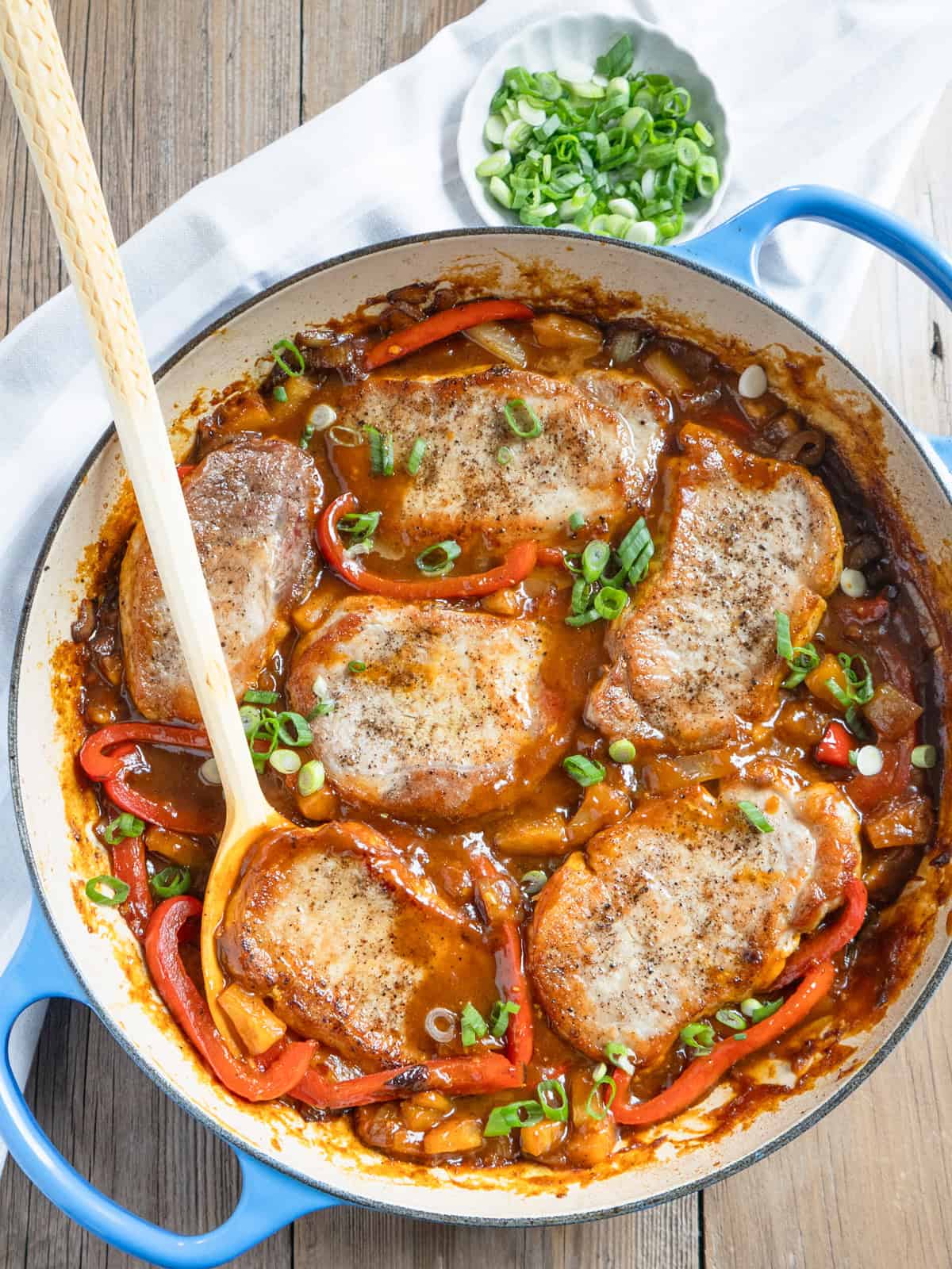 Boneless pork chops in a sweet and sour pineapple sauce with a wooden serving spoon.