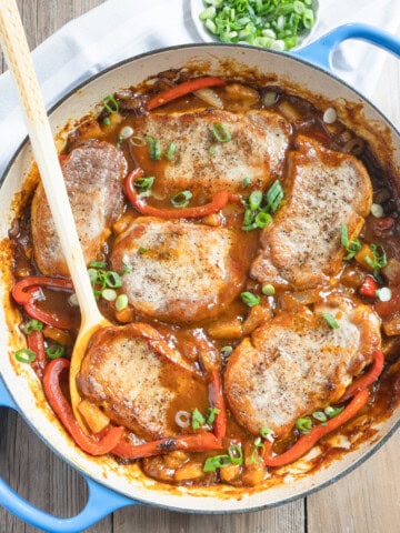 Boneless pork chops in a sweet and sour pineapple sauce with a wooden serving spoon.