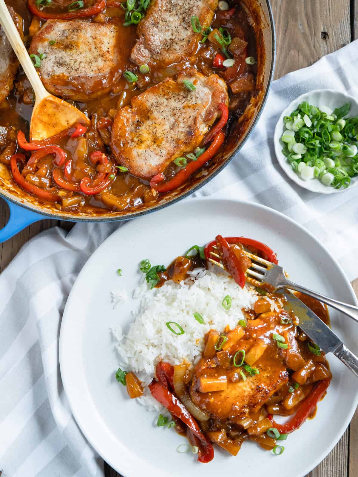 One serving of pineapple pork chops on a plate with rice with the full pan off to the side.