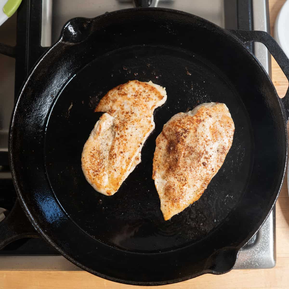 2 chicken cutlets searing in a cast iron pan.