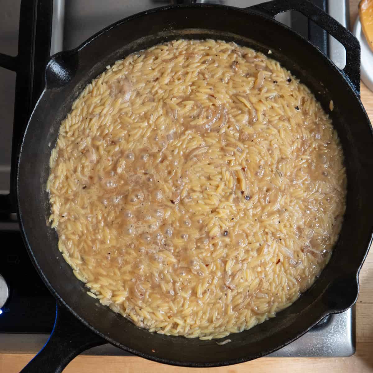 Orzo and chicken broth simmering in a skillet.