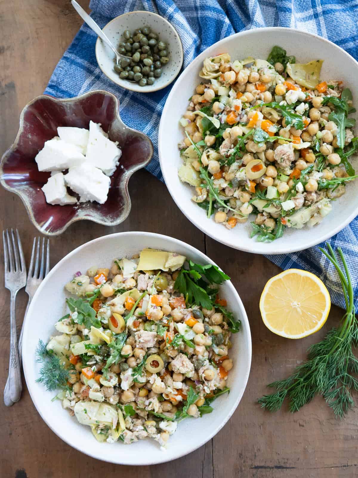Two bowls of chickpea tuna salad garnished with fresh herbs and a dish of feta cheese on the side.