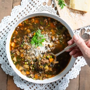 One bowl of beef and vegetable soup with a spoonful of soup being lifted out of the bowl.