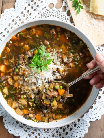 One bowl of beef and vegetable soup with a spoonful of soup being lifted out of the bowl.