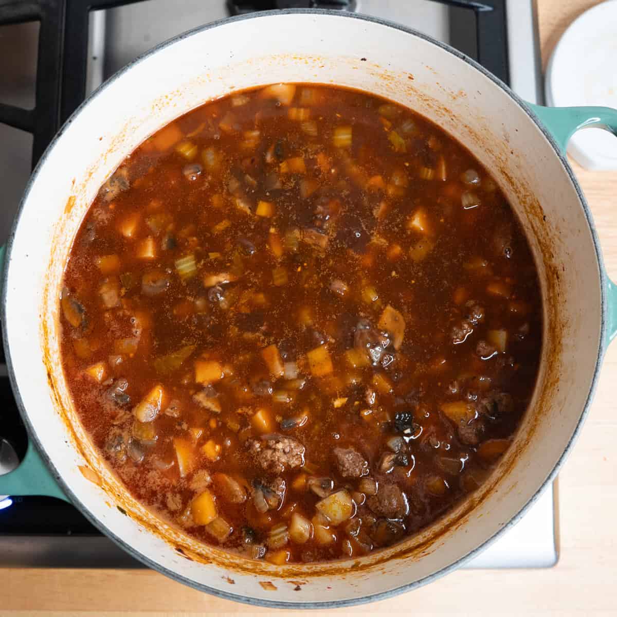 Ground beef, vegetables and broth simmering in a large soup pot.
