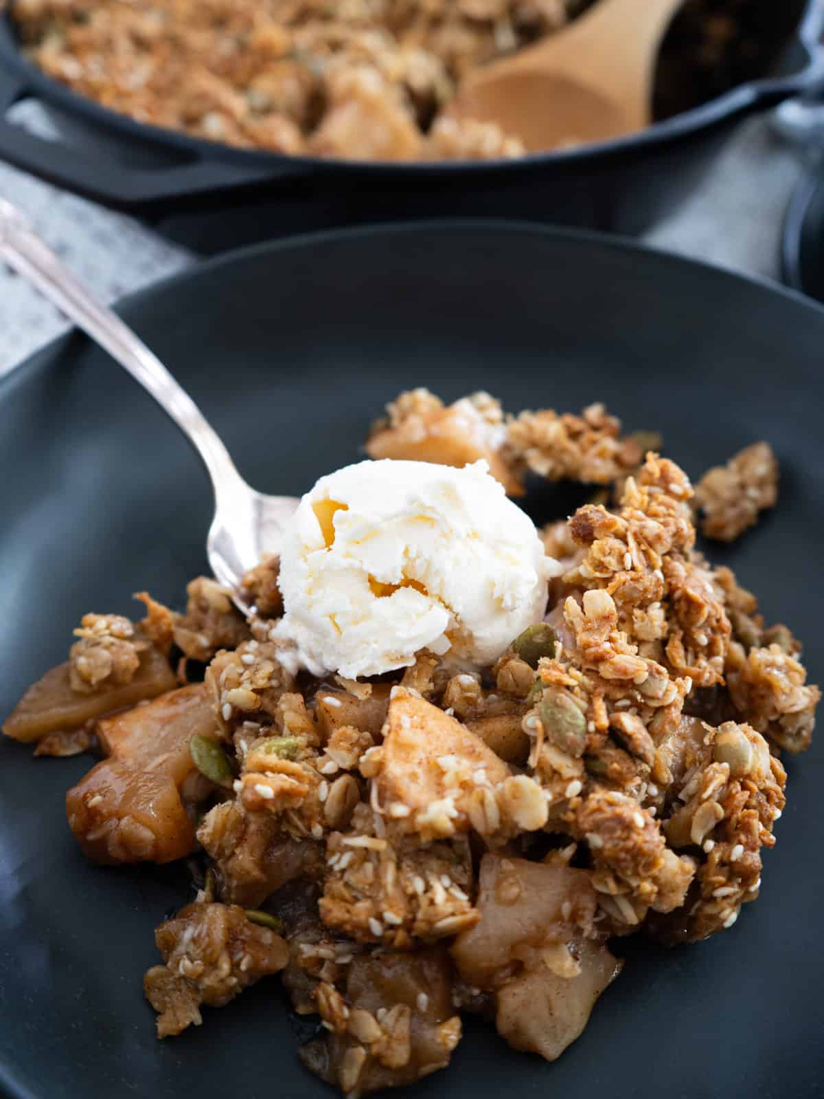 One serving of apple crisp in a black bowl topped with a scoop of ice cream.